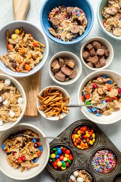 several bowls filled with cereal and candy on top of a white counter next to a wooden spoon