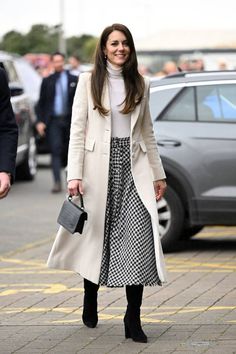 a woman in a white coat and black and white dress is walking down the street