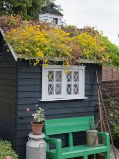 a green bench sitting in front of a black building with flowers growing on it's roof