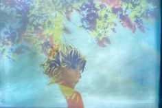 a young boy standing under a tree with his hair blowing in the wind