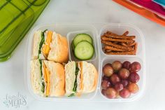 a plastic container filled with sandwiches, grapes and pretzels next to some pickles