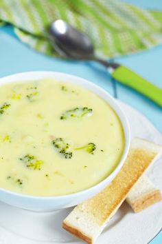 a bowl of broccoli cheese soup on a plate with two slices of bread