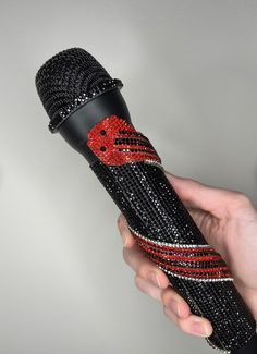 a hand holding a microphone with red and black sequins on the top, in front of a gray background