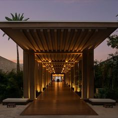 an outdoor covered walkway with benches and lights at dusk in front of the entrance to a resort