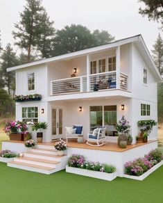 a white house with lots of windows and flowers on the front porch, stairs leading up to the second floor