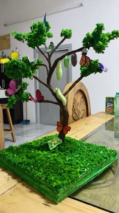 a tree made out of green grass on top of a wooden table with butterflies flying around it