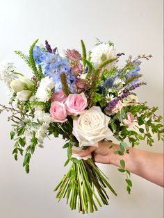 a person holding a bouquet of flowers in their hand with white, pink and blue flowers