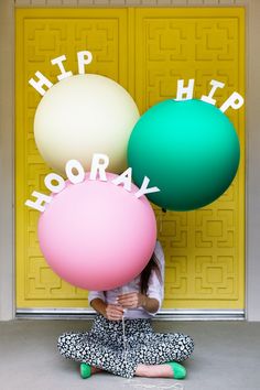 a woman sitting on the floor with balloons in front of her and words that spell hip hooray