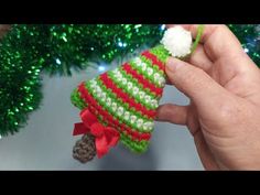 a hand holding a small christmas ornament in front of a green and red tree