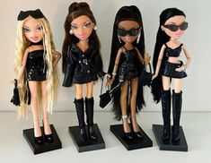 four dolls are standing on black bases with long hair and wearing cat - eye glasses