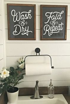 two bathroom signs hanging above a sink with flowers in the foreground and toilet paper on the wall