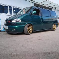 a green van parked in front of a building with gold rims on it's tires