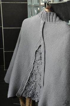 a gray knitted shawl hanging on a hook in front of a tiled wall