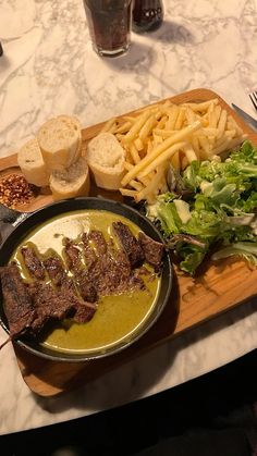 steak, french fries and salad on a wooden platter at a table with glasses of water