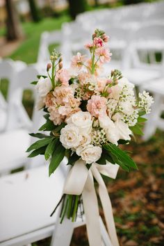 a bouquet of white and pink flowers sitting on top of a wooden chair in the grass