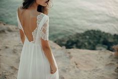 a woman standing on top of a rocky cliff next to the ocean wearing a white dress