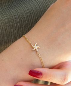 14K Solid Gold Starfish Bracelet This bracelet is a perfect blend of elegance and ocean-inspired charm. Featuring a dainty starfish charm bedazzled with sparkling cubic zirconia stones, this bracelet captures the beauty of the sea. With an adjustable length, it ensures a perfect fit for any wrist. Whether you're dressing up for a summer event or adding a touch of the ocean to your everyday look, this bracelet is a must-have. It also makes a thoughtful gift for ocean lovers, perfect for birthdays, anniversaries, or any special occasion. Features: * Materials: Patented 14K Solid Gold * Gemstone: Cubic Zirconia * Bracelet Length 18+2 cm / approx. 7+0.8 inches Packaging: You will get your jewelry in a beautiful pink Pharos Jewellery box. This box will protect your precious item during the ship Ocean-inspired Bracelet With Starfish Charm, Ocean-inspired Starfish Charm Bracelet, Elegant Starfish Bracelets For Beach, Elegant Starfish Bracelet For Gift, Yellow Gold Starfish Jewelry In Ocean-inspired Style, Yellow Gold Starfish Ocean-inspired Jewelry, Ocean-inspired Starfish Yellow Gold Jewelry, Gold Ocean-inspired Starfish Bracelets, Starfish Charm Bracelet As A Gift