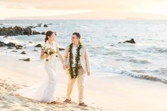 a bride and groom walking on the beach at sunset with leis around their necks