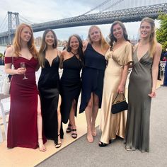 four women are posing for a photo in front of the water with a bridge in the background