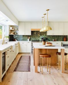 a kitchen with white cabinets and gold pendant lights hanging from the ceiling over an island