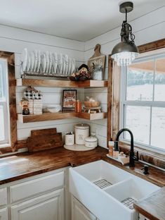 a kitchen with wooden shelves and white dishes on the counter top, next to a window