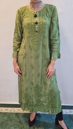 Soft and Rich Muslin Silk Kurta with ruffle at the hem and sleeves. Delicately embroidered in chikankari with self threadwork. Side slits for comfort. Full sleeves. Handmade tassels. Length - 49 inches Color - Olive Green Size -  S - fits bust 34 M - fits bust 36 L - fits bust 38 XL - fits bust 40 0X - fits bust 42 1X - fits bust 44 2X - fits bust 46 Spring Green Dress With Chikankari Embroidery, Green Chikankari Embroidered Dress For Spring, Spring Festive Kaftan With Chikankari Embroidery, Embroidered Green Straight Kurta Tunic, Embroidered Straight Kurta Tunic In Green, Green Embroidered Straight Kurta Tunic, Spring Straight Kurta With Tonal Embroidery, Spring Tunic Kurta With Chikankari Embroidery, Traditional Green Tunic With Floral Embroidery