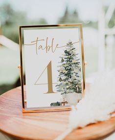 a table number with a christmas tree on it and a white feather sitting next to it