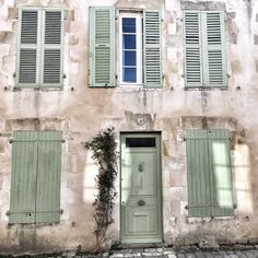 an old building with green shutters on the front and side windows, along with a potted plant