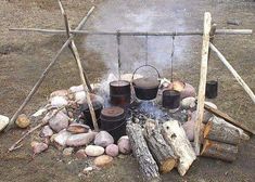 an outdoor fire pit made out of logs and buckets with boiling water on top