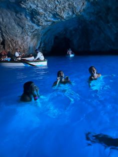 several people are swimming in the blue grotto with boats and canoes near by