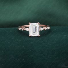 an engagement ring with a emerald stone surrounded by three white diamonds on a green velvet surface