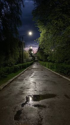 an empty street at night with the moon in the sky and trees on either side