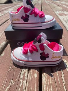 two white shoes with pink bows and minnie mouse heads are sitting on a wooden table