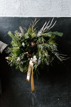 a wreath hanging on the side of a building with gold ribbon and pine cones attached to it