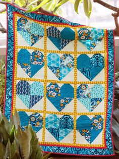 a blue and yellow heart quilt hanging on a tree branch next to a potted plant