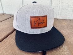 "These adorable hats are completely customizable with  your child's name.  We make our hats with REAL leather and not leatherette.  Due to the nature of natural leather, color maybe slightly different than the color of what is on the screen.  Our 100% polyester/cotton snapbacks are customized with a 100% Full Grain Laser Engraved Leather Patch Hat This is not the fake leather that you see on some of the cheaper hats, each piece of leather is hand stained Sizing: On average our hats will fit chil Adjustable Hats With Leather Patch As Gift, Custom Adjustable Snapback Hat With Flat Bill, Personalized Adjustable Snapback Hat With Flat Bill, Customizable Adjustable Flat Bill Fitted Hat, Custom Adjustable Flat Bill Hat, Adjustable Snapback Hat With Custom Name, Custom Adjustable Flat Brim Baseball Cap, Personalized Adjustable Flat Bill Hats, Flat Bill Hat