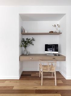 a wooden desk with a computer on top of it in front of a white wall