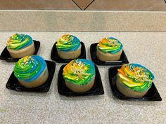 four cupcakes with icing and sprinkles on black trays