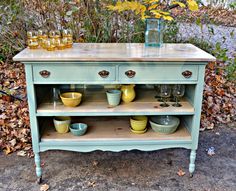 an old dresser is painted blue and has yellow dishes on it, along with glasses