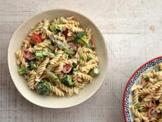 two bowls filled with pasta and vegetables on top of a wooden table next to each other