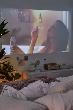 a woman laying in bed while watching a movie on the wall behind her is a potted plant