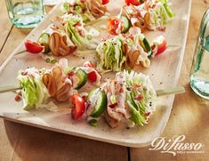 a wooden cutting board topped with lettuce and tomato skewers on top of a table