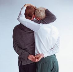 two people hugging each other with their arms around one another, both wearing white shirts and green pants