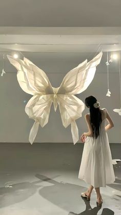 a woman in a white dress looking at a butterfly shaped object hanging from the ceiling