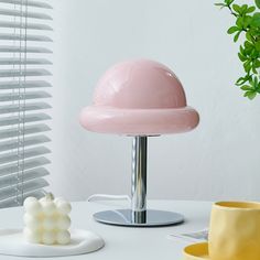 a pink lamp sitting on top of a white table next to a yellow cup and saucer