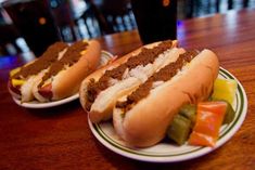 two hotdogs on plates with pickles and peppers