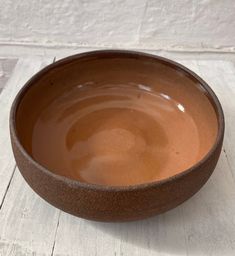 a brown bowl sitting on top of a white wooden table next to a brick wall