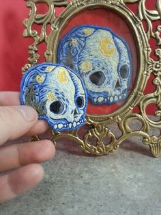 there is a hand that is holding a miniature skull in front of a small mirror