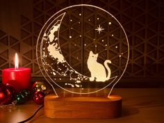 a cat sitting on top of a moon with a candle in front of it next to christmas decorations