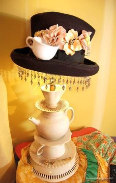 there is a hat on top of a tea pot with flowers in the middle and beads hanging from it